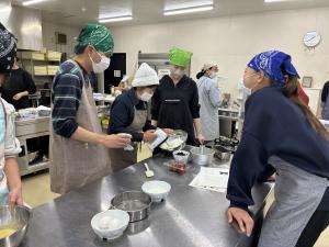 先生からハンドミキサーの使い方を興味津々に学ぶ様子の写真